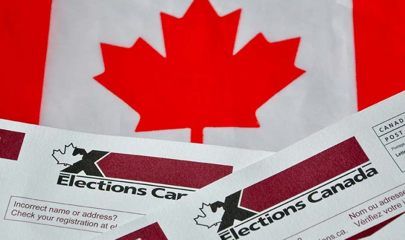A Canadian flag sits behind the top of two voting ballots for Elections Canada