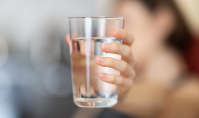 On voit un verre d'eau transparent tenu par une main sur un fond embrouillé