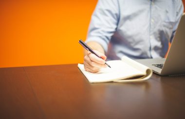 Un homme, entrepreneur est assis et écrit avec un stylo noir sur un block note.