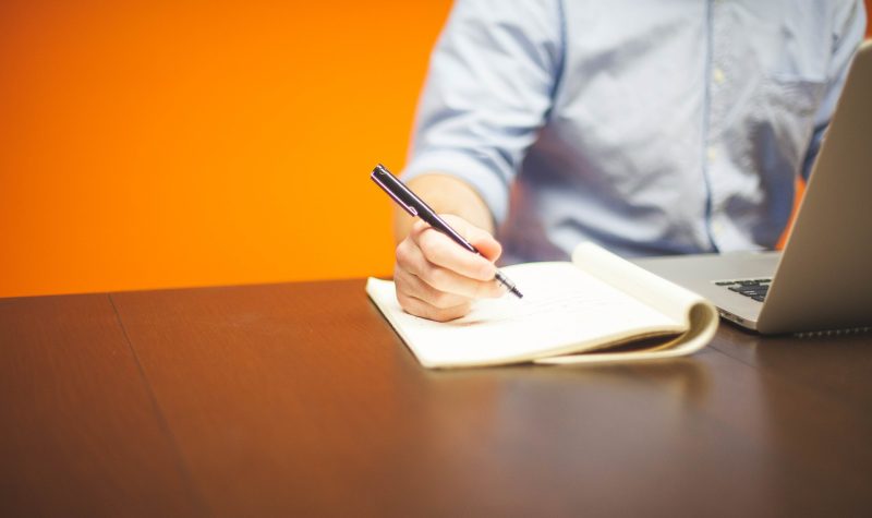 Un homme, entrepreneur est assis et écrit avec un stylo noir sur un block note.