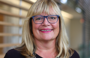 A woman wearing glasses and a necklace smiling