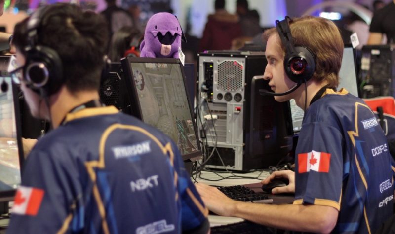 Two people sitting down with headphones on, look at computer screens with CPU towers in the background.