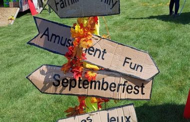 A vertical signpost with cardboard directional arrows pointing to festival activities.