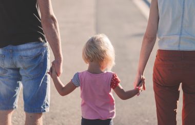 Une petite fille blonde tenant la main de ses 2 parents.