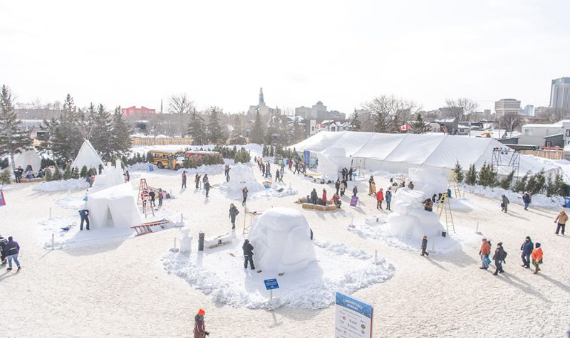 Le parc du voyageur en hiver, une vue élvée, des personnes circulent entre des sculptures de neige.