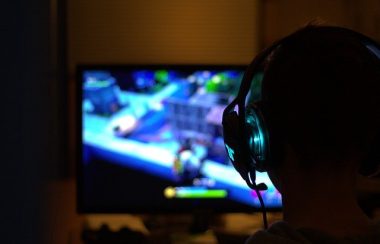 Un jeune enfant joue à un jeu vidéo devant son écran d'ordinateur. L'enfant porte un casque d'écoute.