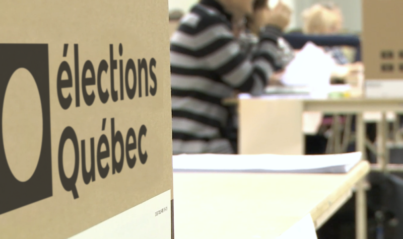 Une portion de boite électorale avec l'inscription Élections Québec et des personnes floues en arrière-plan.