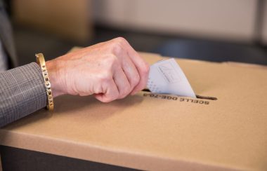 Une main déposant un bulletin de vote dans une urne.