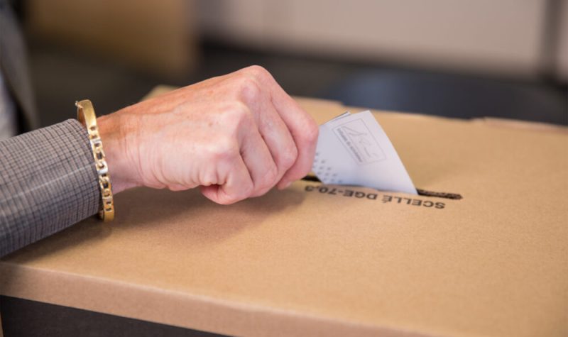 Une main déposant un bulletin de vote dans une urne.