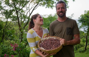 A man and a woman hold a basket of roasted cocoa.