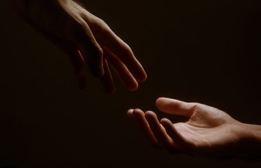 Hands reach out to touch each other against a dark background.