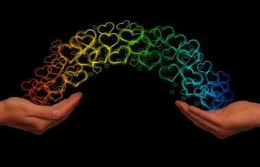 two hands reaching out to eachother. Rainbow hearts are shown making a rainbow between both hands.