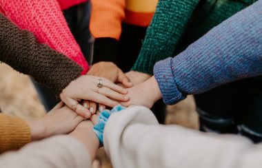 About 10 people's hands overlap in the center.