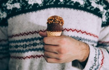 A man's torso dressed in a winter-themed sweater with his hand holding an ice cream cone.