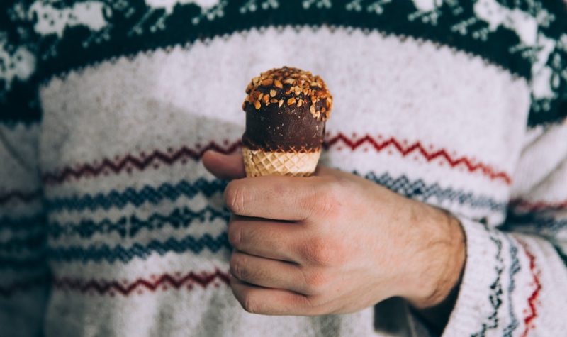 A man's torso dressed in a winter-themed sweater with his hand holding an ice cream cone.