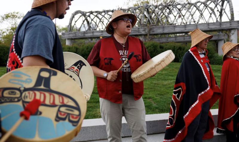 Cultural drumming and dancing by indigenous delegation outside of Harvard Museum. There are four people.