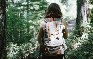 Une femme photographiée de dos, porte un sac à dos dans une forêt