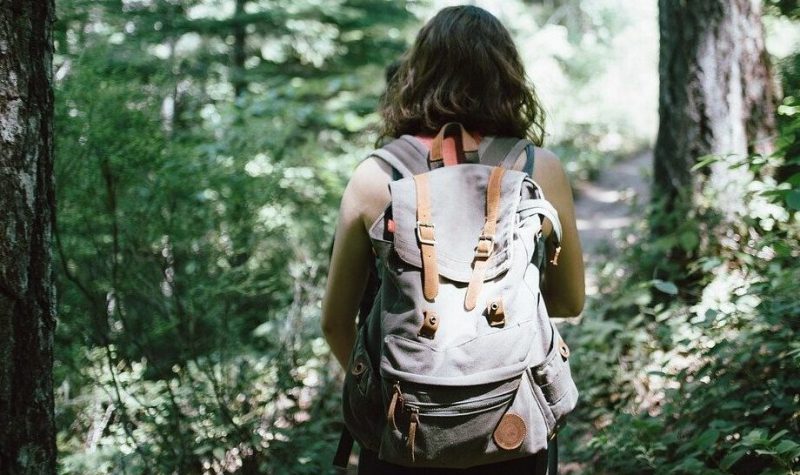 Une femme photographiée de dos, porte un sac à dos dans une forêt