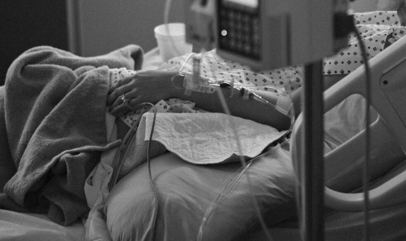 Une main sur un lit d'hôpital branchée sur des appareils médicaux.
