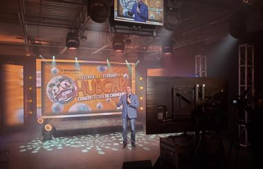 Un humoriste vêtu de bleu devant la scène virtuelle du festival Hubcap