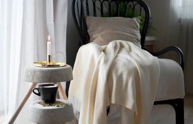 Une chaise sur laquelle jonche une couverture est placée à côté d'une chandelle et une tasse de café.