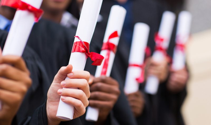 A group of students in gowns hold diplomas in their hands.
