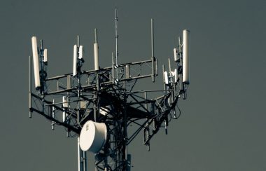 The top of a cellular telecommunications tower against a grey sky.