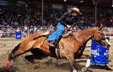 Femme sur une cheval à toute vitesse contournant un baril bleu devant une foule de spectateur