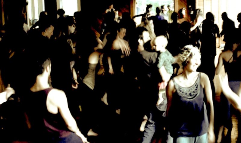 A group of people dance and cast shadows across the crowd.