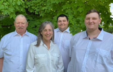 Pictured is a group shot of Chuck Pepler, Jennifer Pepler-Quinn, Alex Beck, and Dilon Elston. They are all wearing white button up dress shirts with greenery serving as the background.