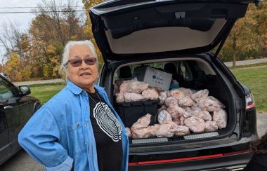 Woman standing beside open trunk of vehicle stuffed with frozen chickens