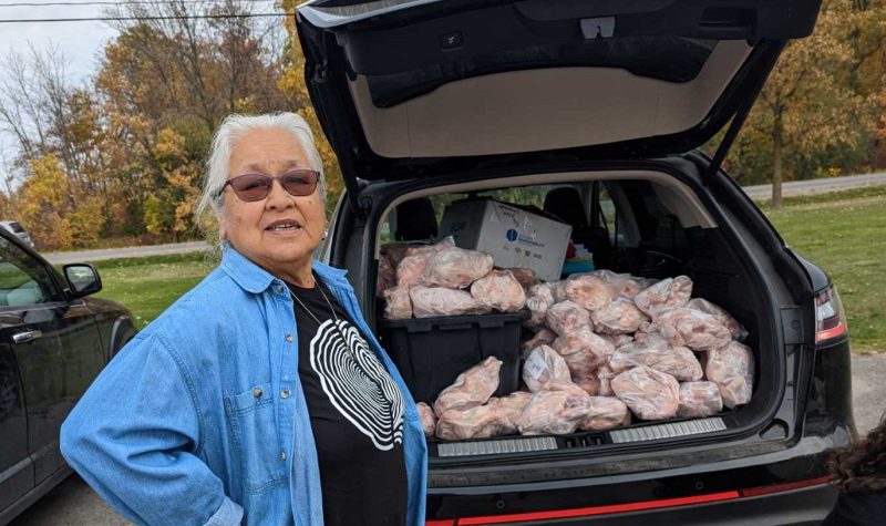 Woman standing beside open trunk of vehicle stuffed with frozen chickens