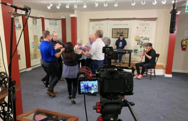 Des gens dansant à la musique d'un violoneux dans un musée.