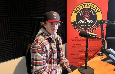 Man sits in front of microphone. Kootenay Co-op Radio poster behind.