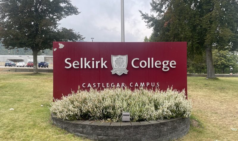 A burgundy sign that says Selkirk College Castlegar Campus. Flowers in front.