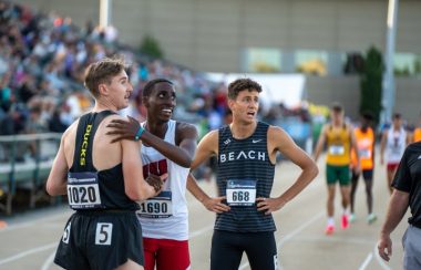 Erickson stands with his back to the camera. A runner from Wisconson has his hands on his shoulder. A third runner looks at the time..