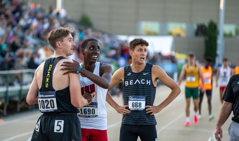 Erickson stands with his back to the camera. A runner from Wisconson has his hands on his shoulder. A third runner looks at the time..