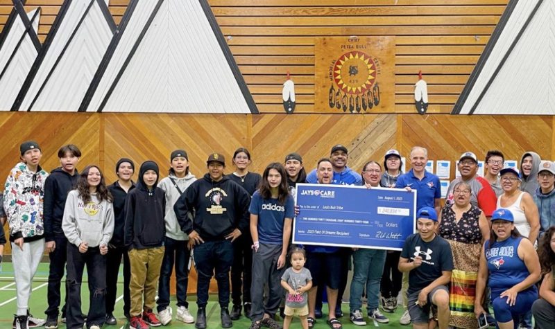 In a gymnasium, a bunch of youth and community members from Louis Bull Tribe and Toronto Blue Jays Care Foundation delegates pose with a big blue cheque.