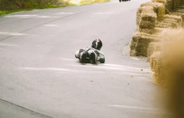 Two people wearing protective equipment riding on the ground next to barrels of hay.