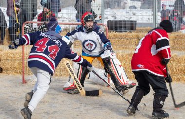 Trois jeunes habillés en jersey jouent au hockey bottine, entouré de balles de foin.