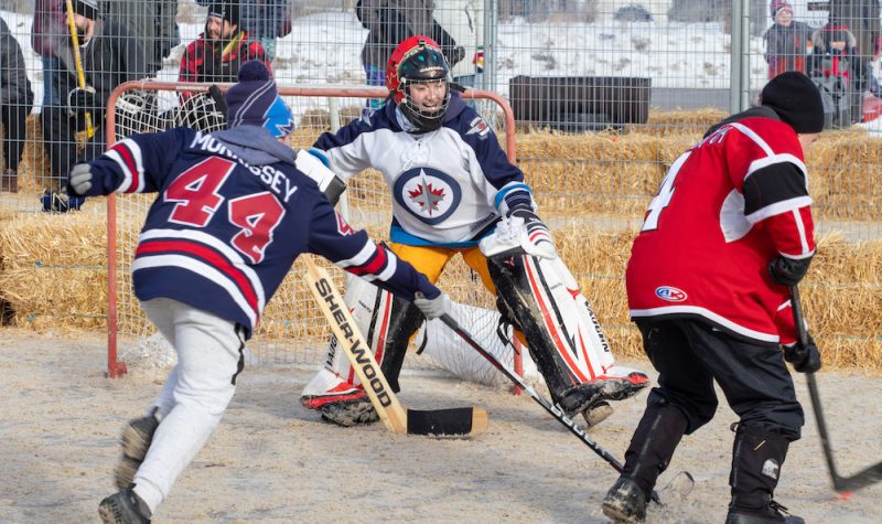 Trois jeunes habillés en jersey jouent au hockey bottine, entouré de balles de foin.
