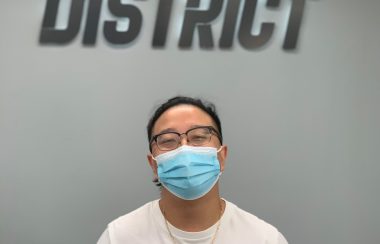 A man with a medical mask standing in front of a wall with a sign on it.