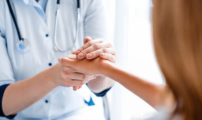 Une infirmière vêtue de bleu tient la main d'une patiente d'une clinique médicale.