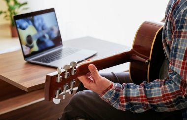 Étudiant qui pratique sa guitar, en lisant des notes sur son ordinateur.