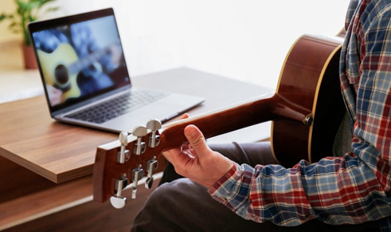 Étudiant qui pratique sa guitar, en lisant des notes sur son ordinateur.