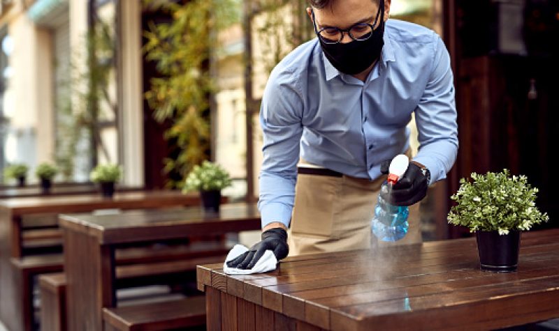 Un homme blanc avec un masque nettoie une table dans un café.
