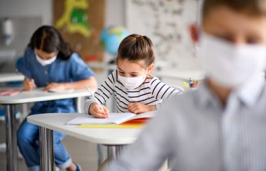 De jeunes élèves portent un masque en salle de classe et écrivent.