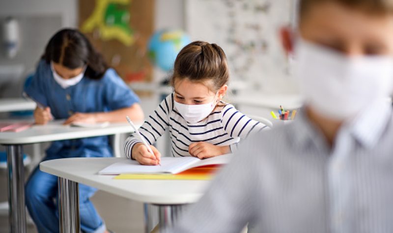 De jeunes élèves portent un masque en salle de classe et écrivent.