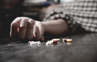 Une main blanche étalée sur le sol entourée d'une boîte de pilule sur le sol.