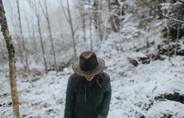 A woman in hat, coat and gloves walks in a snowy forest.